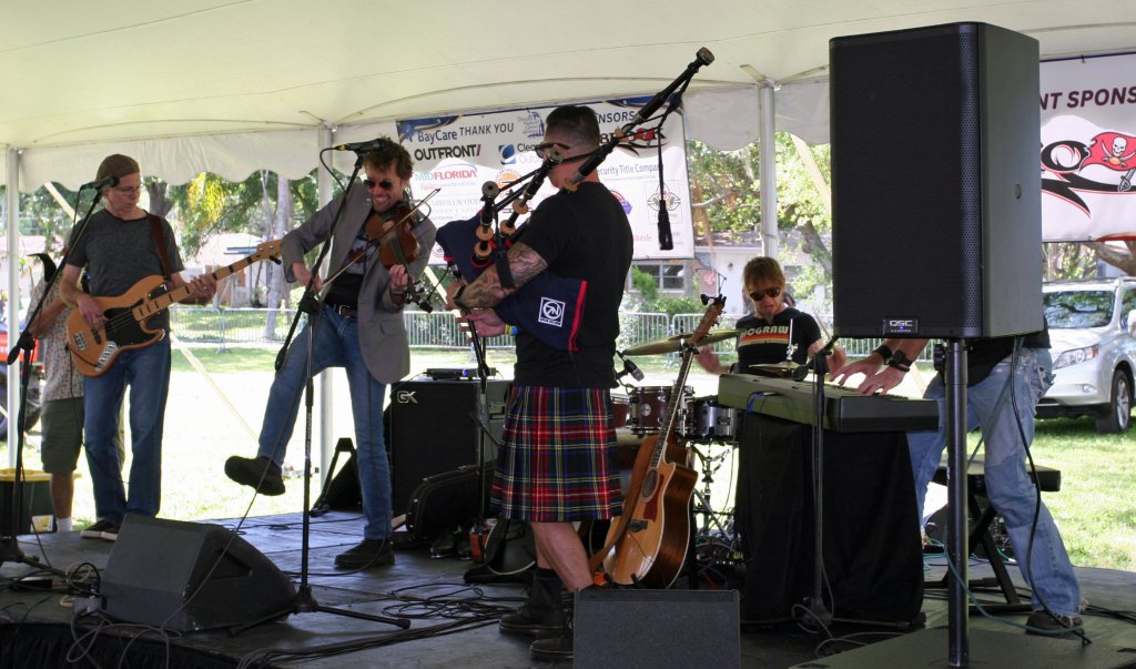 Celtic rock band Seven Nations performs live on stage at the Dunedin Highland Games, featuring a mix of bagpipes, drums, and electric guitars.